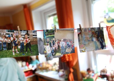 Alte Fotografien sind an einer Schnur aufgehangen. Darauf abgebildet sind Kinder und Events wie z.b. ein Zuckertütenfest. Es sind alte Bilder aus der Kita.