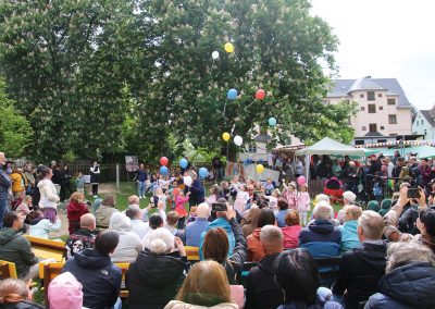 bunte, mit Helium gefüllte Ballons, werden von den Kindern losgelassen und steigen in den Himmel. Der Song von Nena: 99 Luftballons läuft dazu.