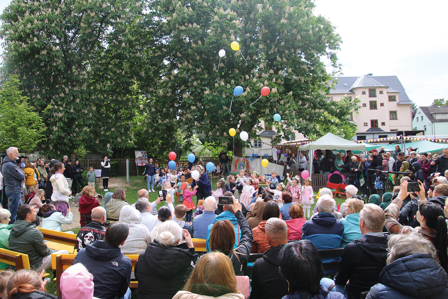 luftballons-steigen-lassen-60-jahre-kita-flax-und-krümel Kinder lassen zum Abschluss des Programmes bunte Luftballons steigen zum Lied 99 Luftballons. Familien und Besucher schauen gespannt zu