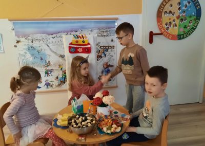 Junge gratuliert Mädchen zum Geburtstag. Kinder sitzen an Geburtstagstisch